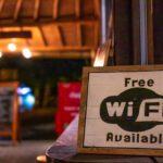 A small, painted wooden sign that says “free Wi-Fi available” in the foreground of a small shop.