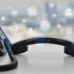 An image of a black phone off the hook with a digital representation of VoIP hanging over the receiver.