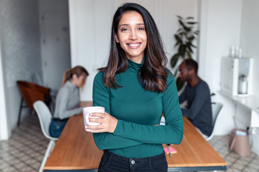A smiling business woman in a green top, holding a coffee cup.