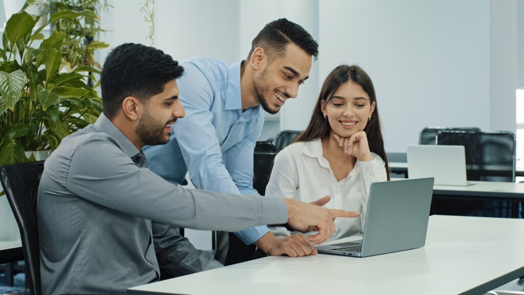 Three co-workers smiling and looking at a laptop screen.