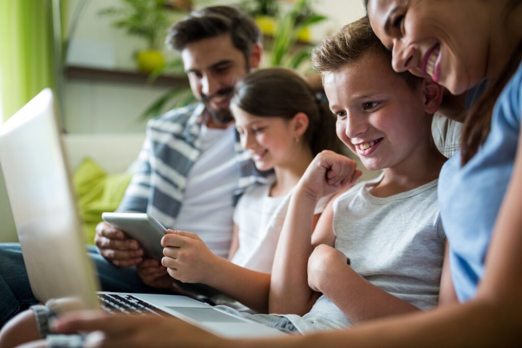 A family sits on the couch using multiple devices to access the internet