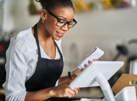 shop assistant placing order from notepad into pos point of sale terminal at register in restaurant