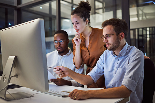 Three workers collaborate on a project while looking at a computer