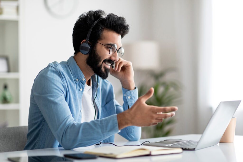 A man talks on a headset while looking at his laptop and working from home