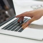 A closeup of a person's hand pressing keys on a white laptop.