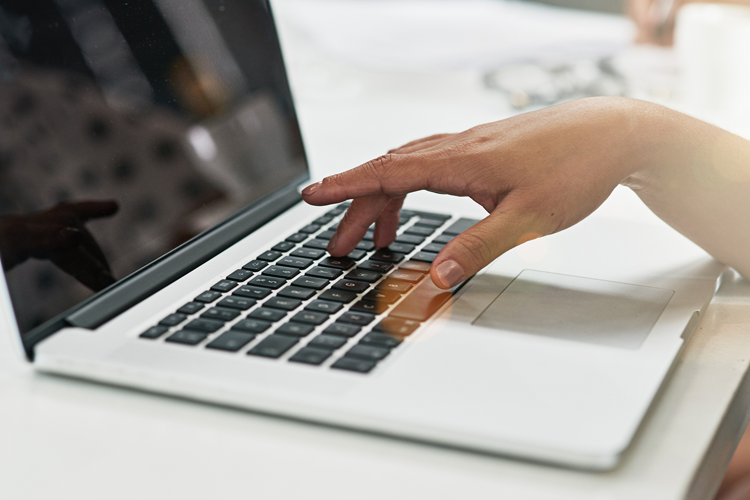 A closeup of a person's hand pressing keys on a white laptop.