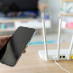 Person holding a smartphone near a Wi-Fi router, possibly setting up or testing a home internet connection.